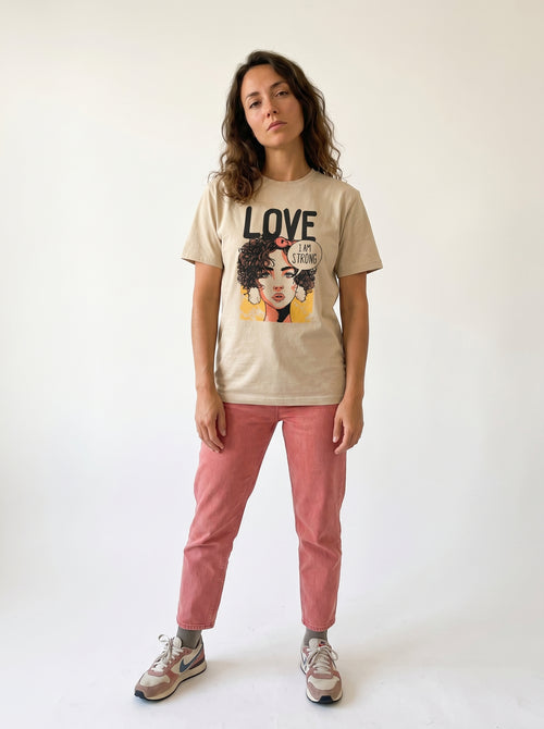 gravisk Love. I Am Strong organic graphic tee. Comic-style portrait with an I AM STRONG speech bubble, LOVE above.