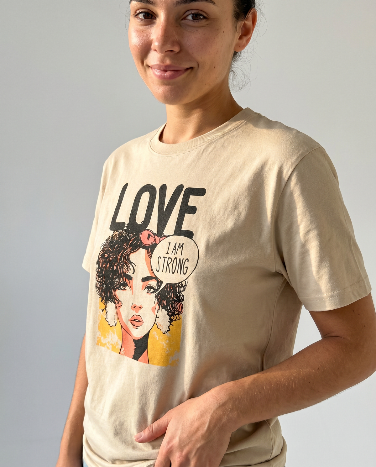gravisk Love. I Am Strong organic graphic tee. Comic-style portrait with an I AM STRONG speech bubble, LOVE above.