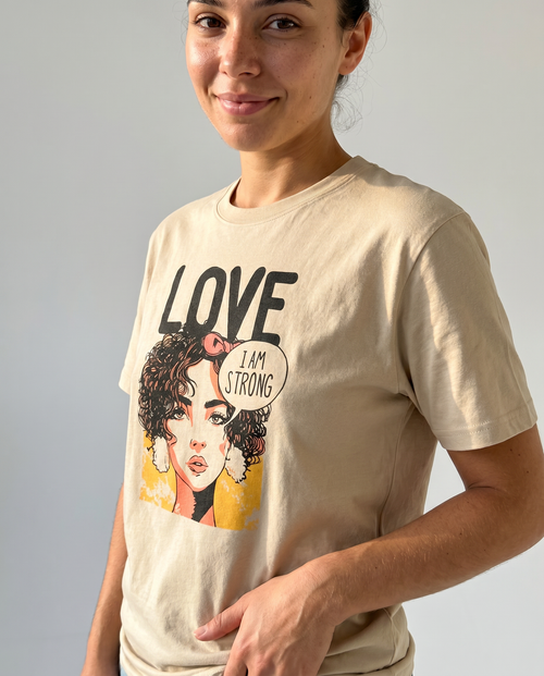 gravisk Love. I Am Strong organic graphic tee. Comic-style portrait with an I AM STRONG speech bubble, LOVE above.