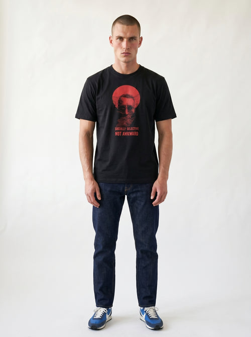 gravisk Socially Selective, Not Awkward organic graphic tee. A man in round glasses, hand over his mouth, inside a red circle.
