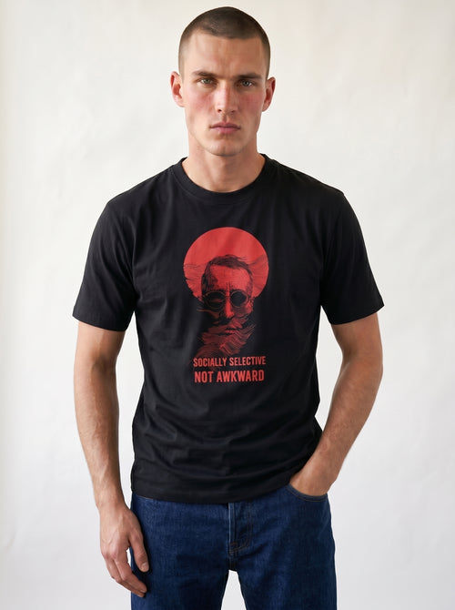 gravisk Socially Selective, Not Awkward organic graphic tee. A man in round glasses, hand over his mouth, inside a red circle.